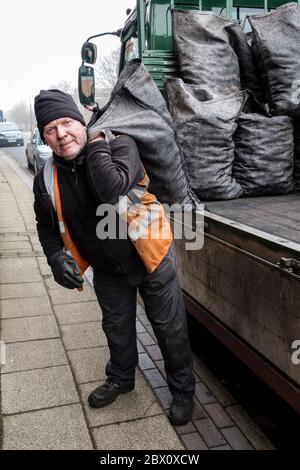 Ein Kohlenmann, der Säcke mit Hauskohle in einer Straße in Longton, Stoke on Trent, Staffordshire, England, liefert Stockfoto