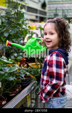 Ein kleines lockiges Mädchen bewässert ihre heimischen Pflanzen Stockfoto