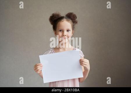 Ein schönes Mädchen mit zwei Schwänzen hält ein weißes Stück Von Papier zum Schreiben Stockfoto