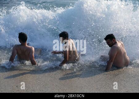 Drei junge Männer sitzen am Meer und fangen Wellen. Stockfoto