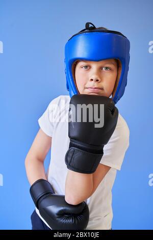 Ein Junge mit grünen Augen trägt einen Boxhelm und Handschuhe auf blauem Hintergrund Stockfoto