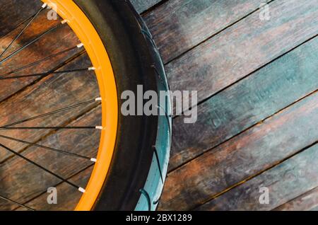 Rad eines stilvollen Fahrrads mit oranger Felge und Gummireifen-Abdeckung, Holzhintergrund Stockfoto