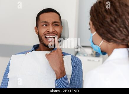 Schwarzer Kerl Besuch Zahnarzt, zeigt Arzt schmerzhafte Zähne Stockfoto