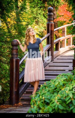 Wunderende junge blonde Frau auf einer Holzbrücke im Herbst japaneese Garten Stockfoto