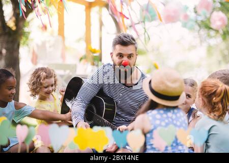 Mann mit kleinen Kindern auf dem Boden im Garten im Sommer, Gitarre spielen. Stockfoto