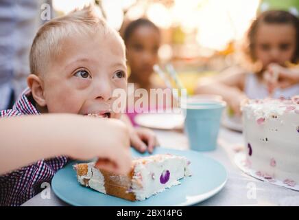Down-Syndrom Kind mit Freunden auf Geburtstagsfeier im Freien, Essen. Stockfoto