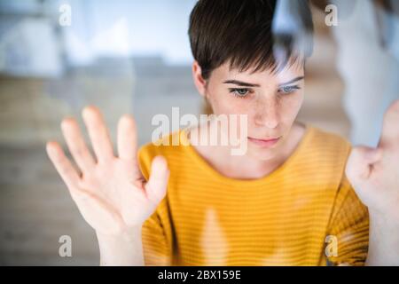 Vorderansicht der traurigen jungen Frau, die zuhause drinnen steht und die Kamera anschaut. Stockfoto