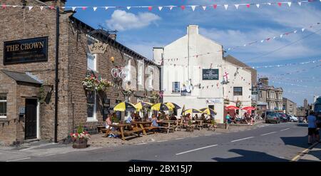 Besucher sitzen an einem sonnigen Sommertag vor den Crown and Fountain Pubs im Zentrum der kleinen Stadt Hawes in Yorkshire Dales Stockfoto