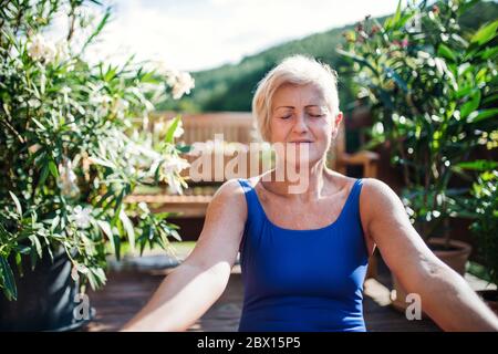 Eine ältere Frau, die im Sommer draußen auf einer Terrasse sitzt und Yoga-Übungen macht. Stockfoto