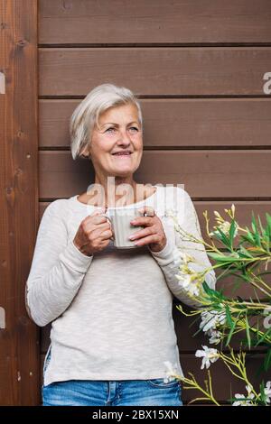 Eine ältere Frau mit Kaffee im Freien auf einer Terrasse im Sommer. Stockfoto