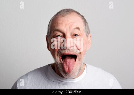 Porträt eines fröhlichen älteren Mannes in einem Studio, herausstehende Zunge. Stockfoto