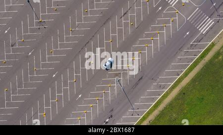 Ein graues Auto fährt durch einen großen leeren Parkplatz mit vielen leeren Parkplätzen. Von oben mit einer Drohne aufgenommen. Stockfoto