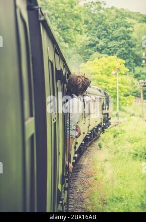 Rückansicht von hinten aus der Nähe des isolierten Zugwachtwachtposten, der sich aus dem fahrenden alten britischen Dampfzug Severn Valley Railway lehnt und schaut. Vintage Railway UK. Stockfoto