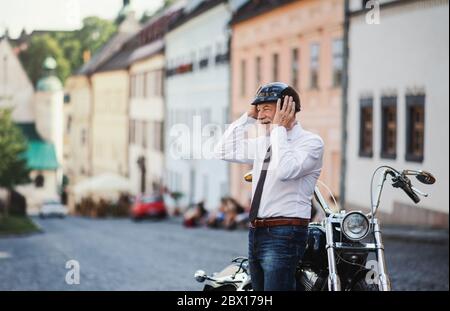 Ein älterer Geschäftsmann mit Motorrad in der Stadt, der Helm aufsetzt. Stockfoto