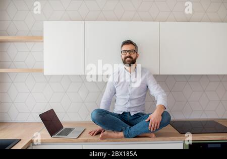 Ein reifer Mann mit Laptop sitzt in der Küche in unmöbliertem neuen Haus. Stockfoto