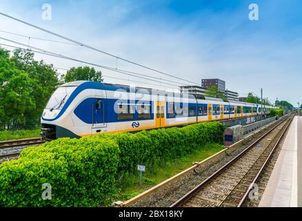 Amsterdam, Niederlande, Mai 22 2017: Holländischer Zug, der an einem kleinen Bahnhof im westlichen Teil von Amsterdam vorbeifährt Stockfoto