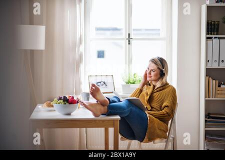 Junge Frau, die zuhause am Tisch sitzt und ein Buch liest. Stockfoto