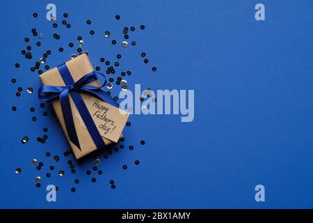Alles gute zum Vatertag Konzept. Geschenkbox mit blauer Schleife und Konfetti auf blauem Hintergrund Draufsicht. Vorlage für Grußkarten zum Vatertag. Stockfoto