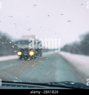 Verschwommener Blick durch die Windschutzscheibe in den Regentropfen auf der Autobahn, die sich in Richtung eines großen Autos bewegt. Selektiver Fokus Stockfoto