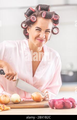 Junge Frau mit einem unglücklichen Gesichtsausdruck schneidet Zwiebel mit einem Messer. Stockfoto