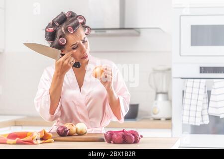 Mädchen weint über Zwiebelhacken in der Küche mit Kopfwicklern in der Küche. Stockfoto