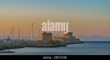 Berühmte Windmühlen und Festung im Mandraki Hafen, Rhodos, Griechenland bei Sonnenuntergang. Stockfoto