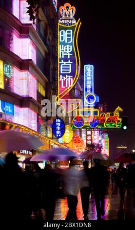 Shanghai, China, Asien - Neon-Zeichen an der Nanjing Road, der wichtigsten Handelsstraße der Stadt und Menschen unter dem Regen. Stockfoto