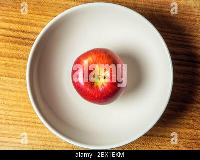 Ein einzelner Braeburn, der einen Apfel in einer großen Schüssel von oben auf einem Holzhackbrett isst Stockfoto