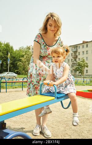 Aktives kleines Mädchen auf dem Spielplatz. Spielendes Kind mit Mutter auf einer Schaukel. Stockfoto