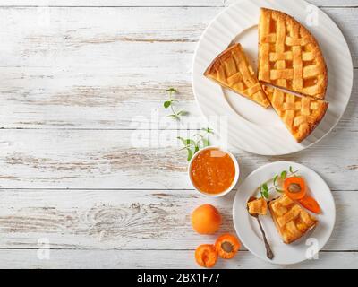 Geschnittene Aprikose-Mürbeteig mit einem Gitter-Tortenkruste auf weißen Tellern auf einem rustikalen Holztisch, flache Lage, Freiraum Stockfoto