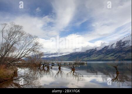 Die Weiden des Lake Wakatipu und Glenorchy Wharf, Otago, Neuseeland. Magische Szene im Winter mit bewölktem Himmel, Bergen und Bäumen im Wasser reflektiert Stockfoto