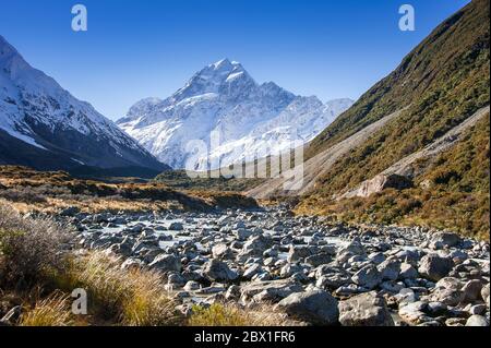 Der Gletscherbach fließt durch eine felsige Landschaft im Hooker Valley, Mount Cook National Park. Tasman River Valley mit Blick auf einen schneebedeckten Gipfel Stockfoto