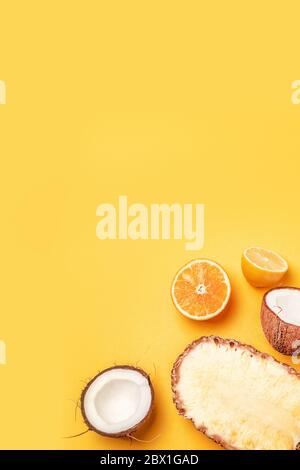 Leckere Hälften von exotischen Früchten Ananas, Kokosnuss, Orange, Zitrone auf gelbem Hintergrund. Vertikales Foto, Draufsicht mit Kopierbereich Stockfoto