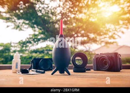 Schwarze spiegellose Kamera mit Objektiv, das mit Kamera-Reinigungs-Kits im Hintergrund auf einem Holztisch befestigt ist. Kamera- und Objektivpflege. Stockfoto