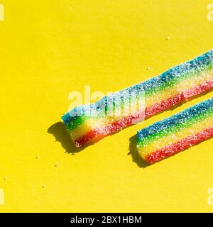 Gestreifte, bunte Marmelade im Zucker auf gelbem Hintergrund. Regenbogenfarbene Marmelade Süßigkeiten. Kopierbereich, leere Vorlage für Text Stockfoto
