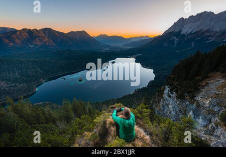 Frau mit Blick über den Eibsee und das Zugspitzmassiv mit Zugspitze, Sonnenaufgang, Wettersteinkette, bei Grainau, Oberbayern, Bayern, Deutschland Stockfoto