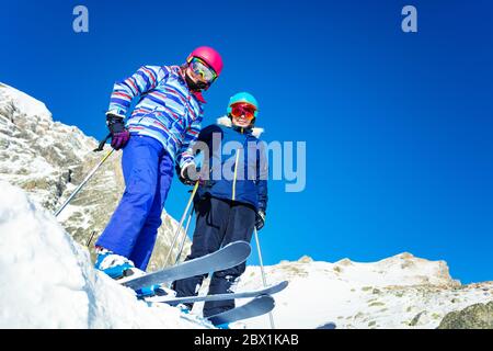 Zwei Mädchen stehen auf dem Gipfel des Berges auf einem Schneehaufen, Blick von unten mit Ski- und Skiausrüstung Stockfoto