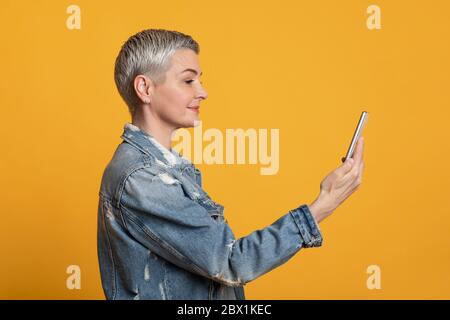 Biometrische Identifizierung. Moderne lächelnde Frau mittleren Alters mit Smartphone-Scan Gesicht in App Stockfoto