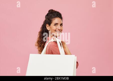 Porträt von glücklichen jungen Frau lächelnd an der Kamera und hält weiße Papiertasche isoliert auf rosa Hintergrund Stockfoto