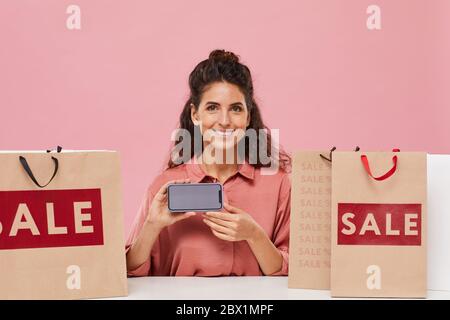 Porträt der jungen glücklichen Frau mit lockigen Haaren lächelnd auf Kamera und zeigt den Bildschirm ihres Mobiltelefons sie Online-Shopping Stockfoto