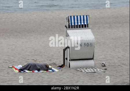 04. Juni 2020, Mecklenburg-Vorpommern, Kühlungsborn: Eine Frau liegt in einer Decke gewickelt neben einem Liegestuhl. Dicke Wolken und sinkende Temperaturen lassen jedoch für die meisten Urlauber kein Strandwetter zu. Foto: Bernd Wüstneck/dpa-Zentralbild/dpa Stockfoto