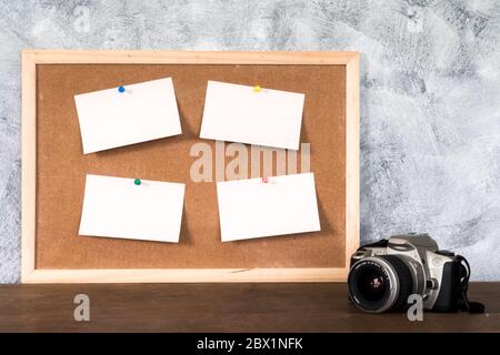 Leere Papiere stecken auf Korkplatte und Kamera über Holztisch mit texturiertem Hintergrund. Stockfoto