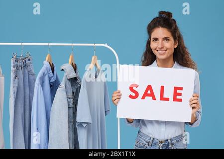 Porträt einer jungen Verkäuferin, die beim Verkauf von Jeans-Kleidung im Geschäft vor der Kamera lächelt Stockfoto