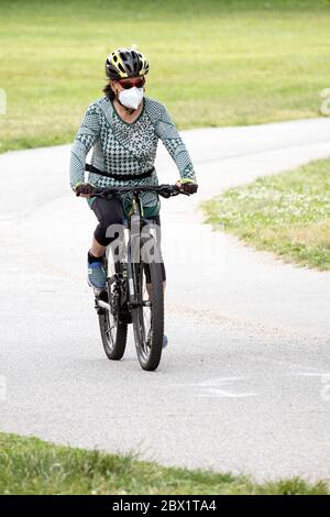 Eine Radfahrerin, die während der Coronavirus-Pest eine chirurgische Maske trägt. Reiten auf dem Weg in Little Bay Park, Whitestone, Queens, New York City Stockfoto