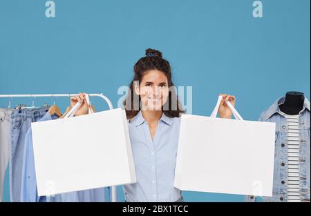 Porträt der jungen glücklichen Frau Kleidung kaufen sie hält Einkaufstaschen in ihren Händen isoliert auf blauem Hintergrund Stockfoto