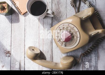 Blick von oben auf die alte Telefon mit Kaffeetasse, Notebook und Kaktus auf weissem Holztisch Hintergrund. Stockfoto