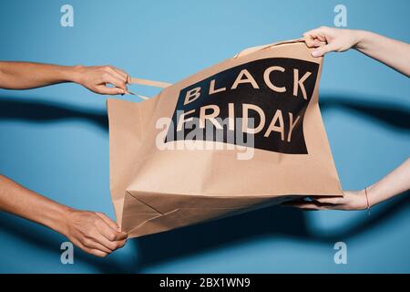 Nahaufnahme von zwei Frauen, die die Papiertüte von Black Friday vor dem blauen Hintergrund ziehen Stockfoto