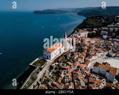 Luftaufnahme auf Piran Stadt mit Tartini Platz, alte Gebäude mit roten Dächern, St. George's Pfarrkirche in der venezianischen Renaissance-Architektur Stockfoto