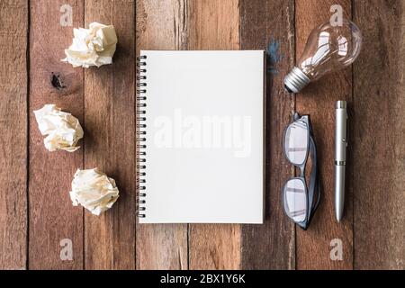 Blick von oben auf die Notebook mit zerknittertem Papier Kugeln, Stift, Brille und Glühbirne auf hölzernen Tisch Hintergrund. Stockfoto