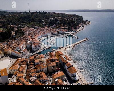 Luftaufnahme auf Piran Stadt mit Tartini Hauptplatz, alte Gebäude mit roten Dächern, der Hafen von Piran mit reflektierenden Booten und Adria in sou Stockfoto